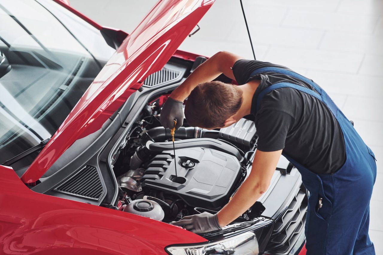 top view of male worker in uniform that repairs red automobile